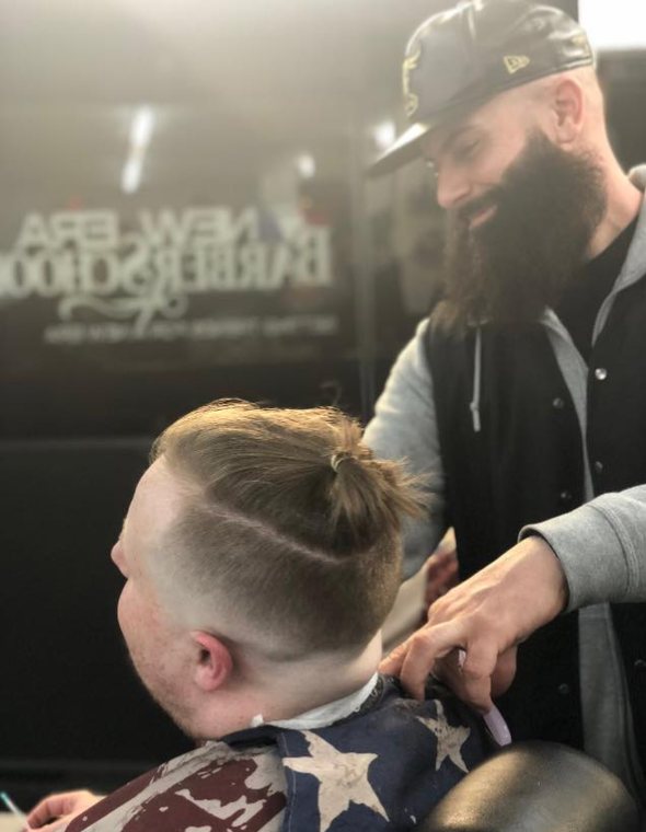 A barber finishing a fade on a young client wrapped in a flag cape